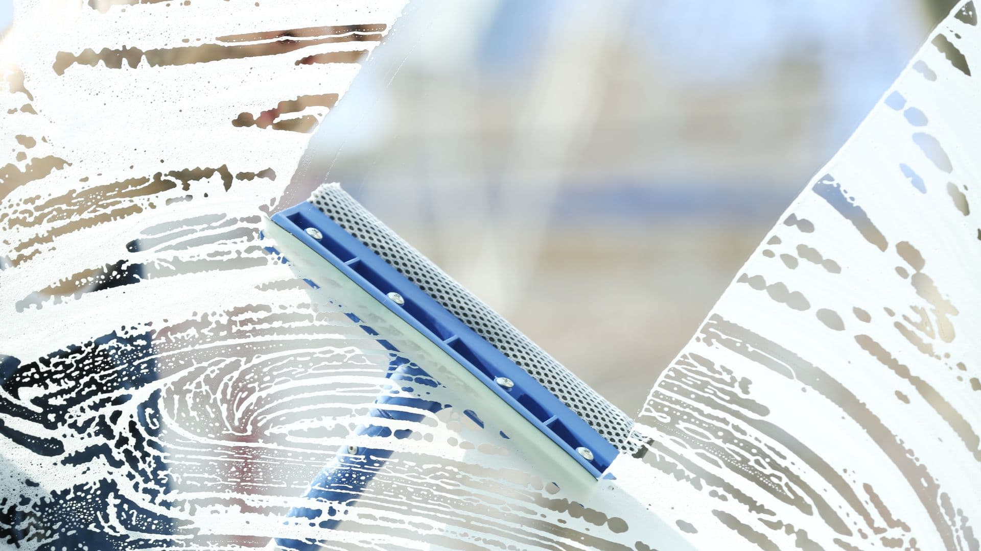Blue squeegee cutting through soap on a window pane