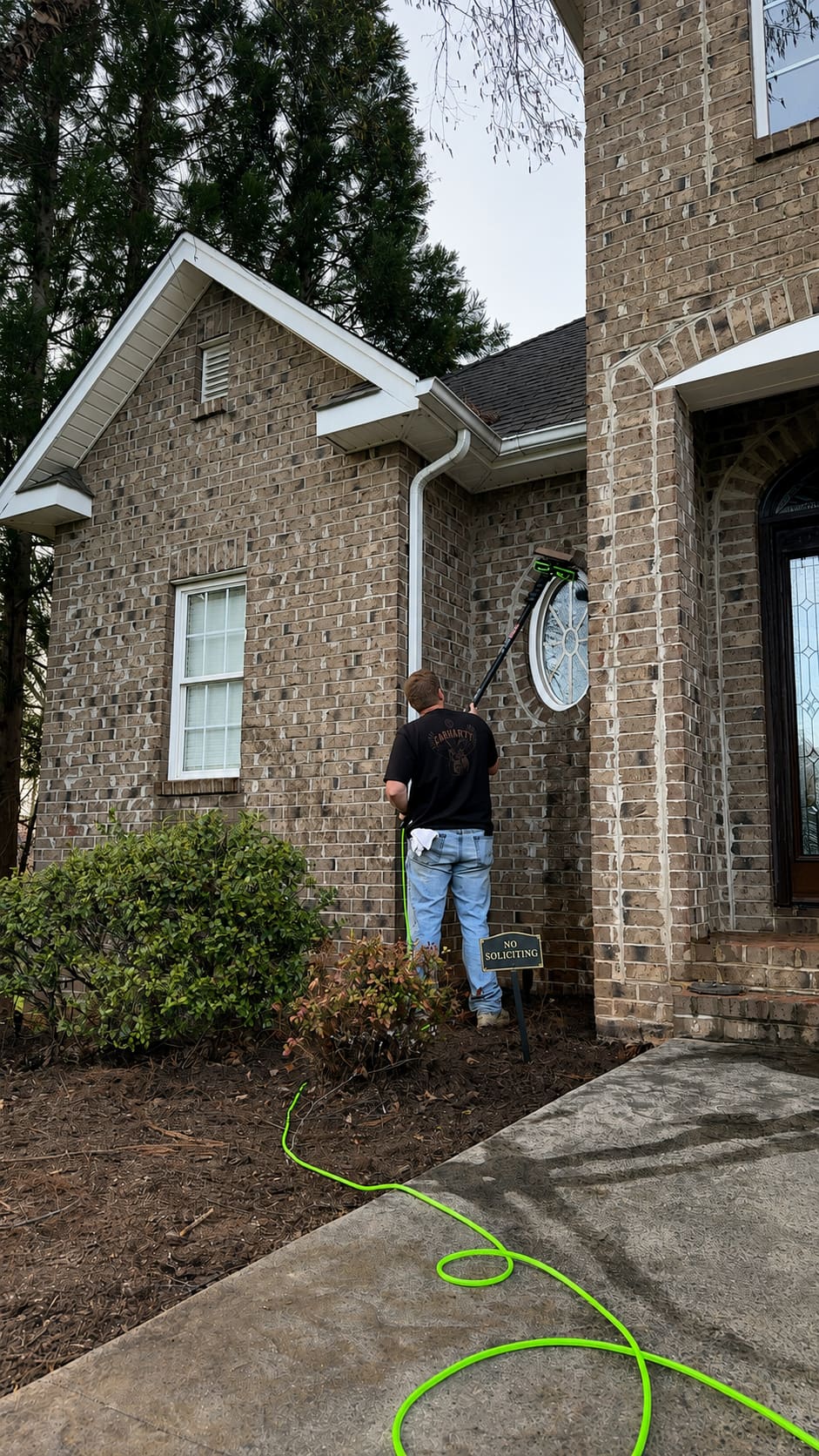 Technician washing an oval accent window with a water-fed pole brush