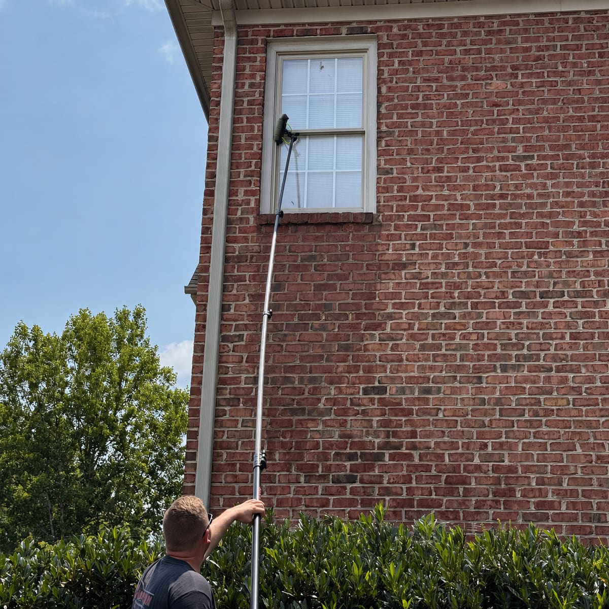 Pure-water pole brush scrubbing an upper window on a two-story brick house