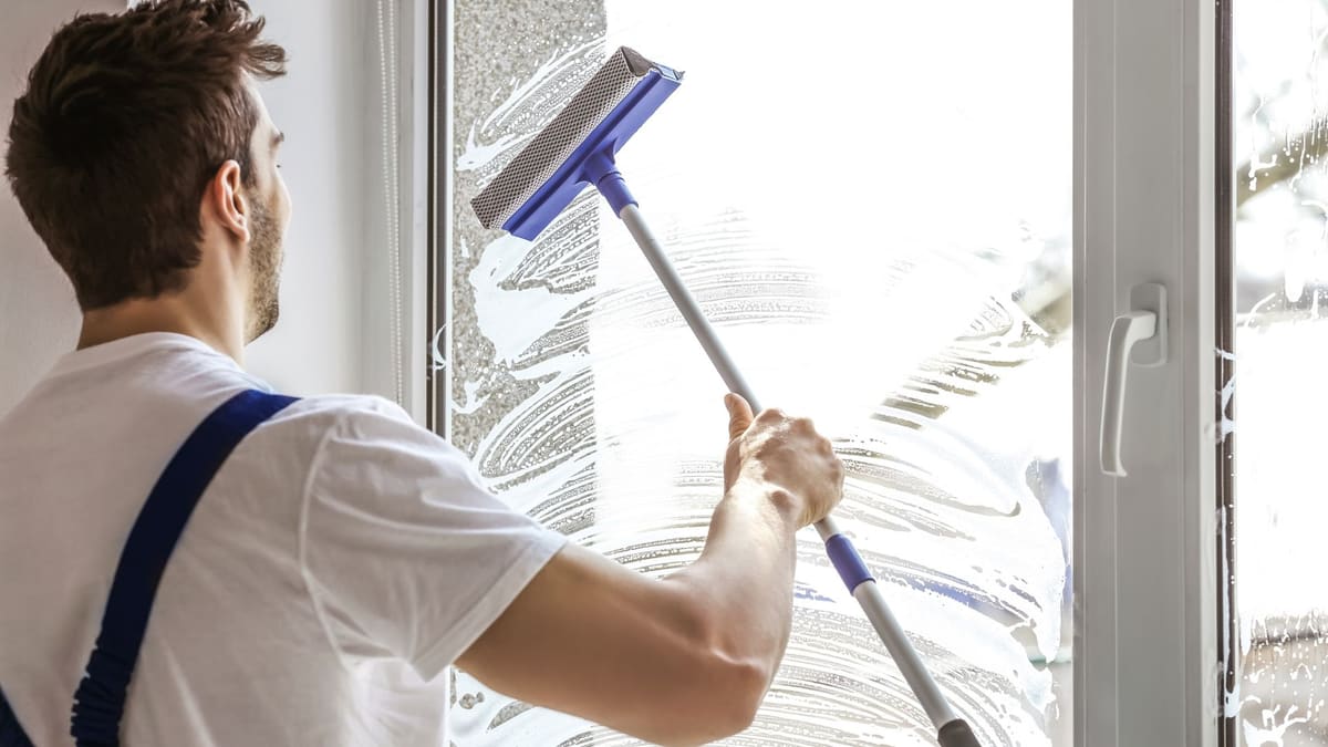 Technician cleaning a tall interior window with an extension squeegee